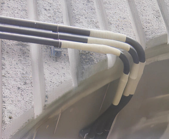 Three black and white insulated cables bundled together and secured with a wire clip against a textured gray concrete or stucco wall.