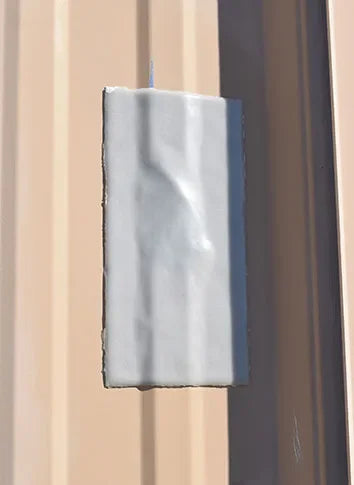 A rectangular white textured panel or tile mounted against a beige wall with a dark vertical trim or door frame visible on the right.